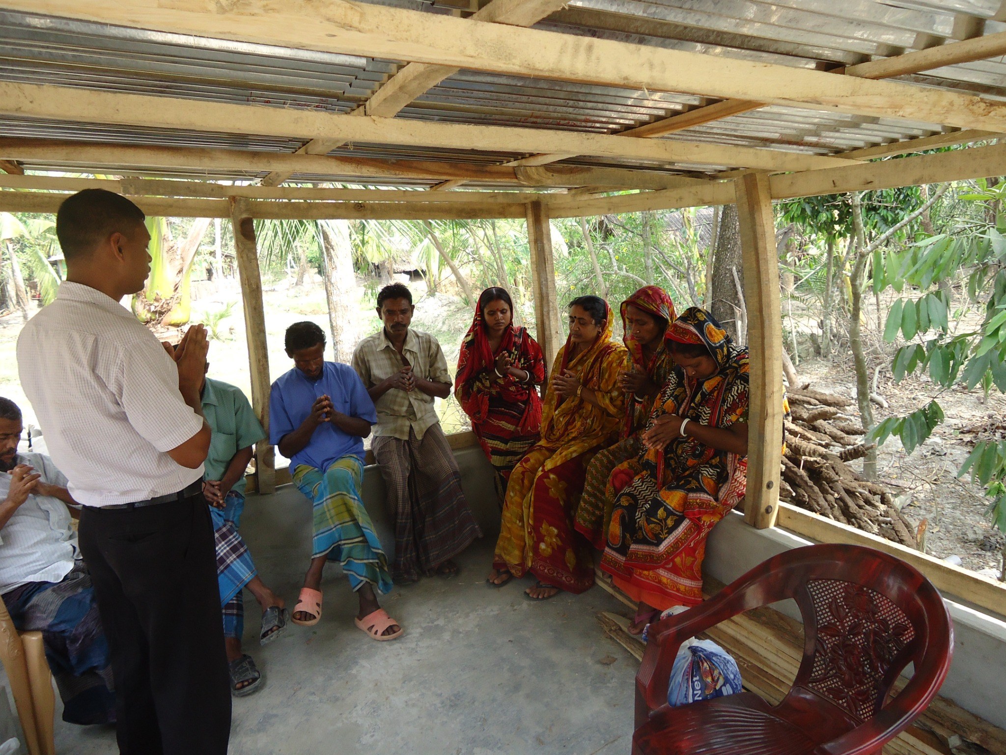 Community members gathered in prayer in a simple village shelter